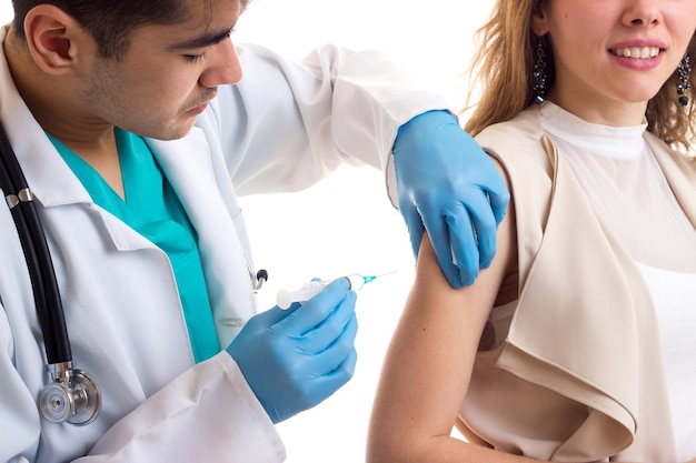 Young handsome doctor in white gown with stethoscope making an injection of young beautiful woman