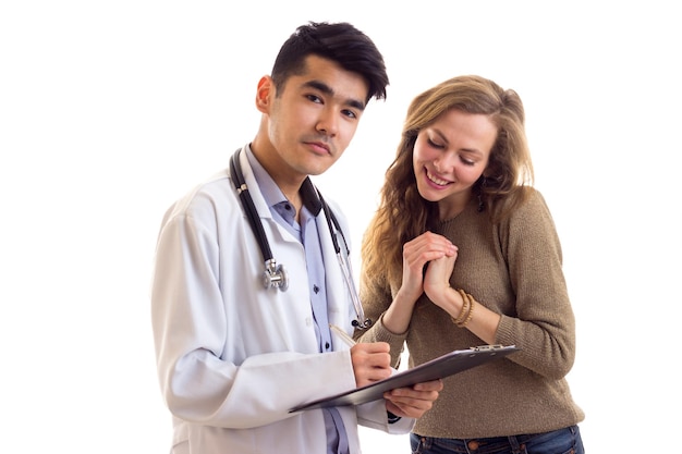 Young handsome doctor with stethoscope writing in a folder and young beautiful woman looking at it