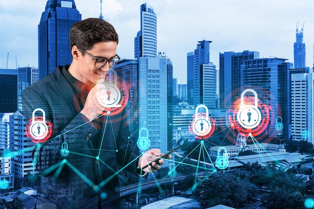 A young handsome eastern cybersecurity developer explores new approaches to protect clients confidential information using phone IT lock icons over Kuala Lumpur city background