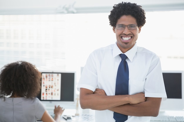 Young handsome editor smiling at camera with colleague working behind him