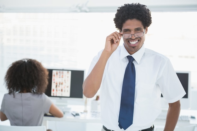 Young handsome editor smiling at camera with colleague working behind him