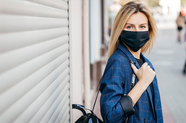 Young handsome fashion woman in sunglasses with backpack in face pollution mask to protect himself from the coronavirus walking in city