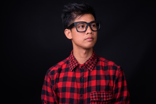  young handsome Filipino hipster man with eyeglasses against black wall