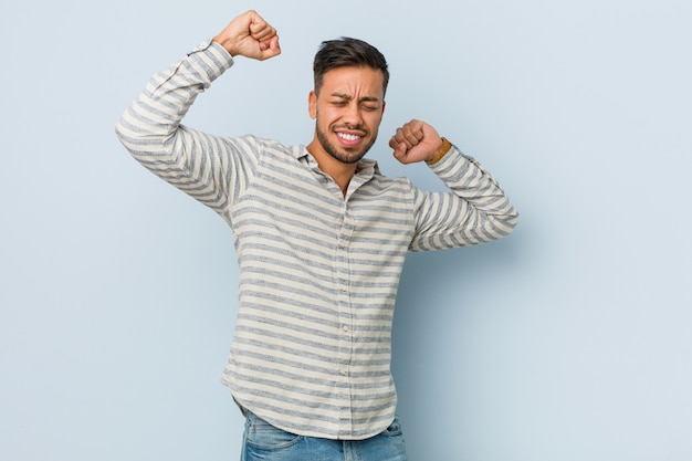 Young handsome filipino man celebrating a special day, jumps and raise arms with energy.