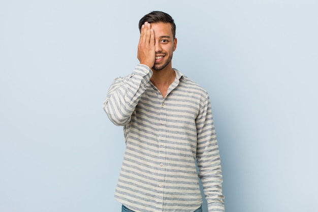 Young handsome filipino man having fun covering half of face with palm.