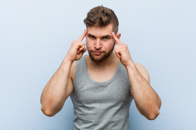 Young handsome fitness man focused on a task, keeping him forefingers pointing head.