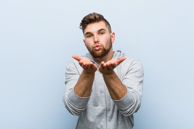 Young handsome fitness man folding lips and holding palms to send air kiss.