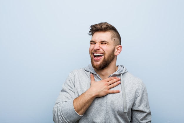 Young handsome fitness man laughs out loudly keeping hand on chest.