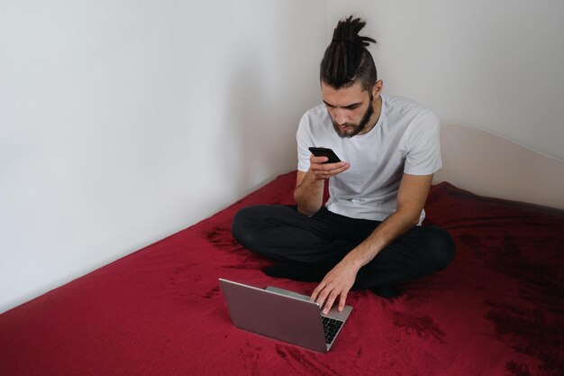 Young handsome freelancer man in white Tshirt with beard and dreadlocks works at home