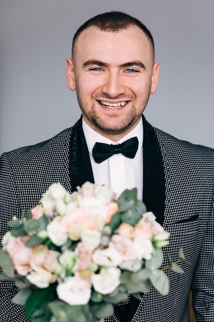 Young handsome groom in a white shirt bow tie jacket going to the wedding ceremony in the morning A man holds a bouquet of flowers