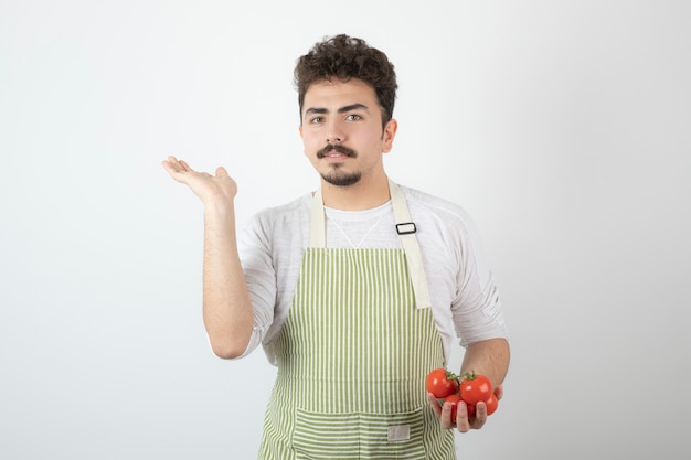 Young handsome guy holding fresh tomatoes and raising hand up.