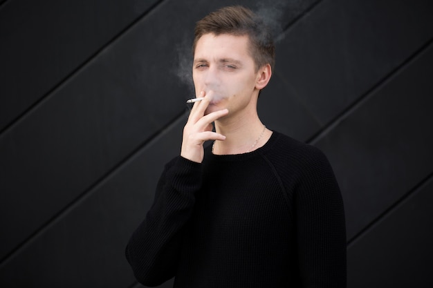 Молодой красивый парень курит сигарету на черном фоне