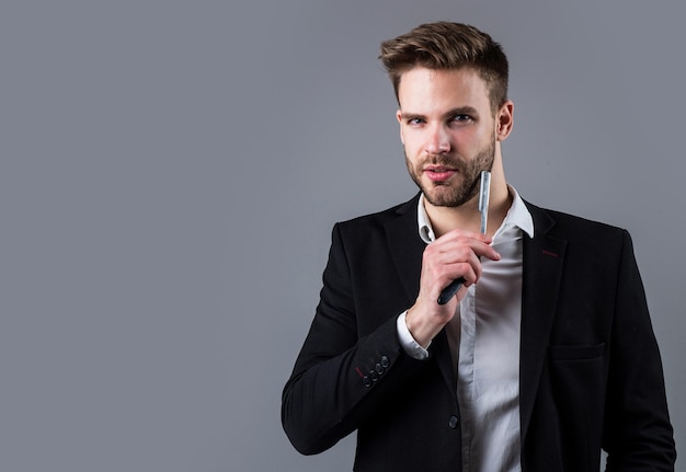 Young handsome guy in suit hold razor blade. male barber master with tool. bearded man with business look. fashion and beauty. barbershop concept. mens hair styling and grooming.