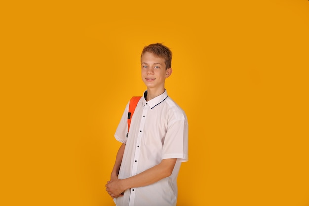 彼の肩にオレンジ色のバックパックと黄色の背景と白いシャツを着た若いハンサムな男