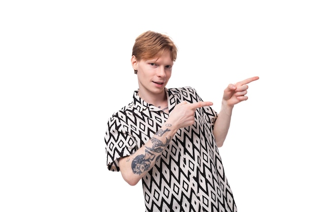 A young handsome guy with red hair and a tattoo on his arms dressed in a shortsleeved shirt points