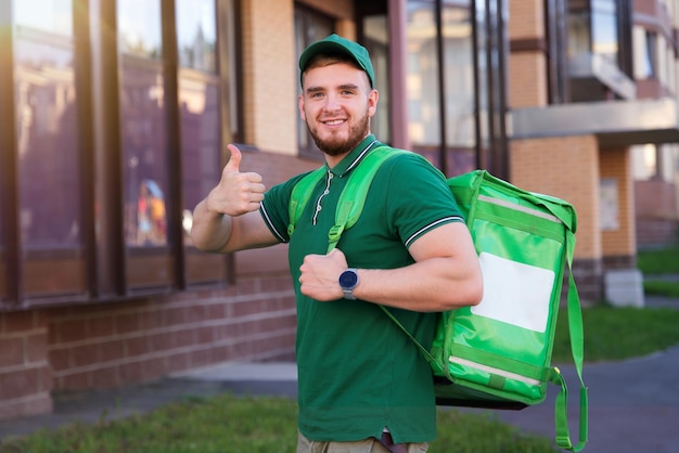 Young handsome happy courier guy, food delivery man with green\
thermo box for food delivering food