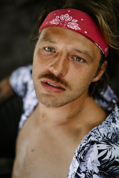 Young handsome hippie man in a red bandana, with a naked torso in a cafe in Bali. Happy man smiling