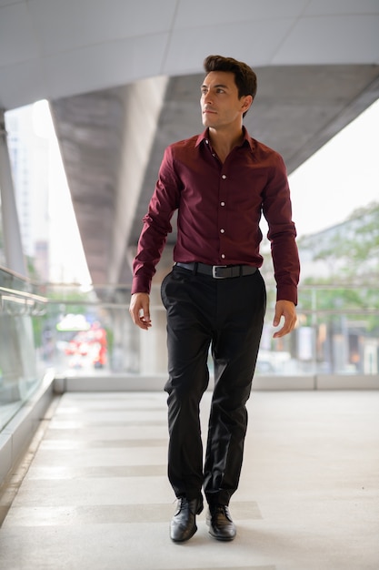 Young handsome Hispanic businessman thinking and walking on the footbridge