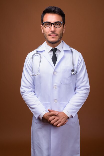 Young handsome Hispanic man doctor against brown background