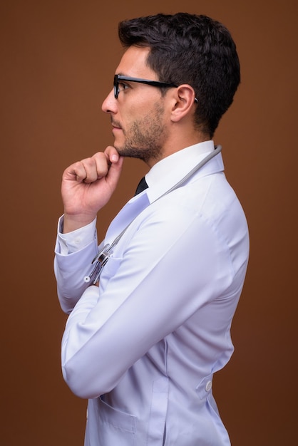 Young handsome Hispanic man doctor against brown background