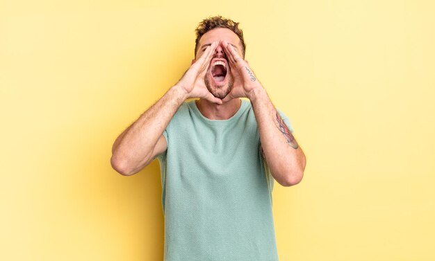 Young handsome hispanic man feeling happy, excited and positive, giving a big shout out with hands next to mouth, calling out