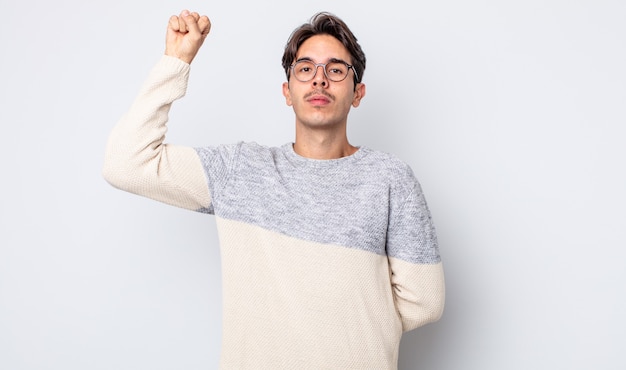 Young handsome hispanic man feeling serious, strong and rebellious, raising fist up, protesting or fighting for revolution