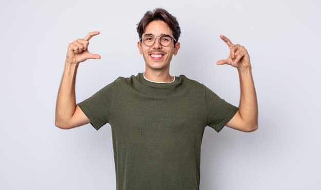 Young handsome hispanic man framing or outlining own smile with both hands, looking positive and happy, wellness concept