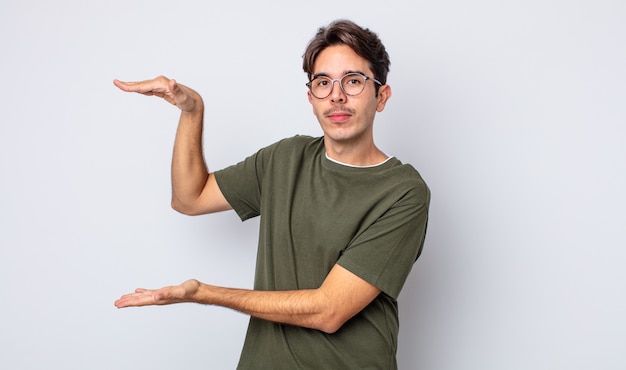 Young handsome hispanic man holding an object with both hands on side copy space, showing, offering or advertising an object