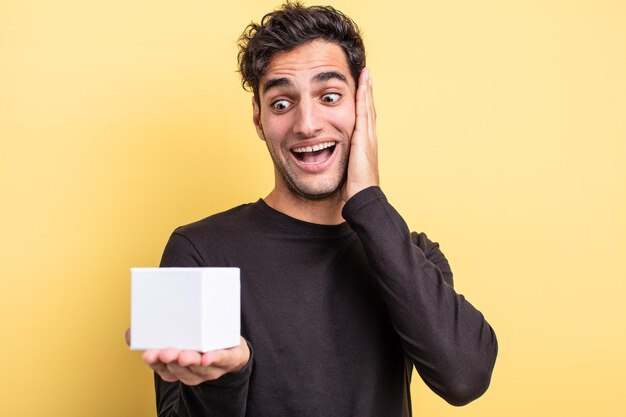 Young handsome hispanic man holding a white box