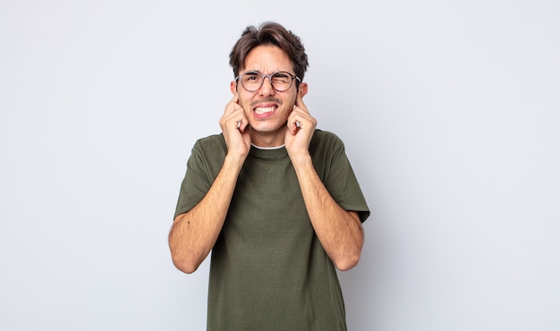 Young handsome hispanic man looking angry, stressed and annoyed, covering both ears to a deafening noise, sound or loud music