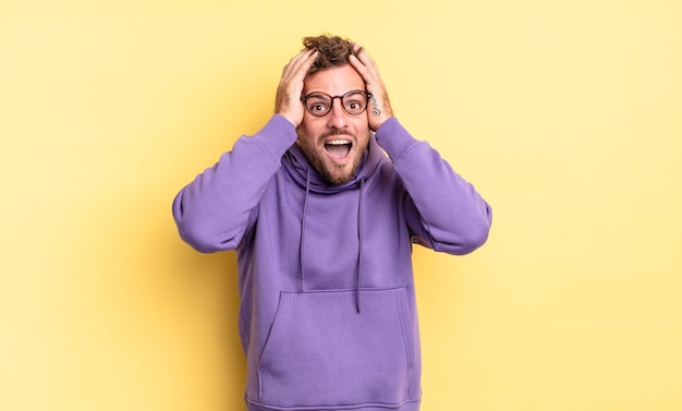 Young handsome hispanic man looking excited and surprised, open-mouthed with both hands on head, feeling like a lucky winner