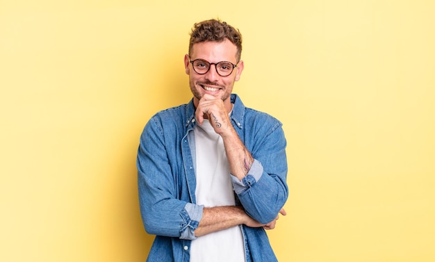 若いハンサムなヒスパニック系の男性は、幸せそうに見えて、あごに手を添えて笑って、疑問に思ったり、質問したり、オプションを比較したりします