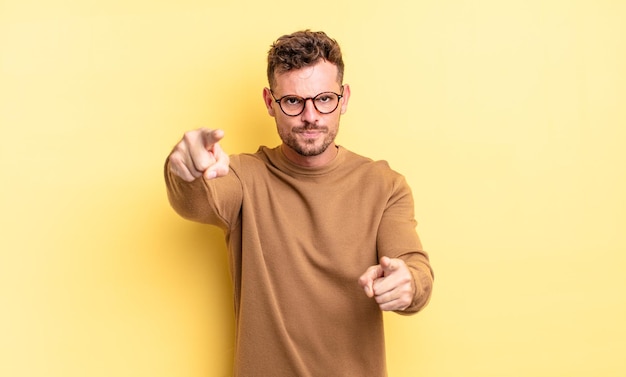 Young handsome hispanic man pointing forward at camera with both fingers and angry expression, telling you to do your duty