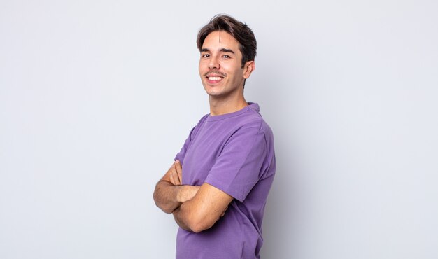 Young handsome hispanic man smiling to camera with crossed arms and a happy, confident, satisfied expression, lateral view