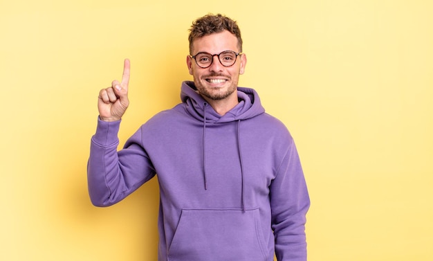 Young handsome hispanic man smiling cheerfully and happily, pointing upwards with one hand to copy space