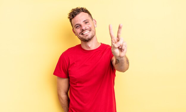 Young handsome hispanic man smiling and looking happy carefree and positive gesturing victory or peace with one hand