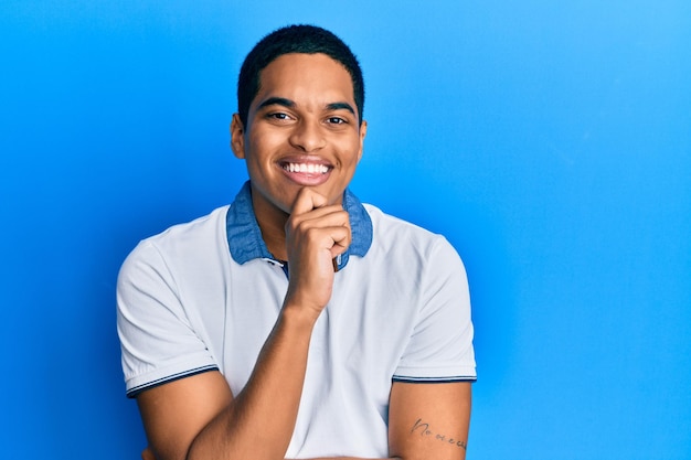 Young handsome hispanic man wearing casual clothes smiling looking confident at the camera with crossed arms and hand on chin thinking positive