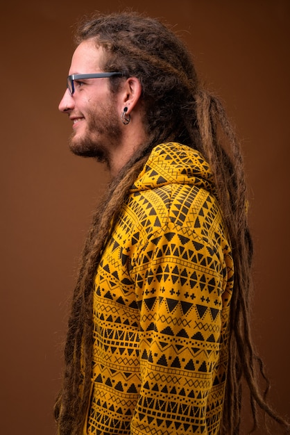 Young handsome Hispanic man with dreadlocks against brown background