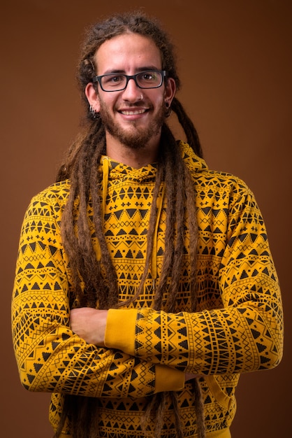 Young handsome Hispanic man with dreadlocks against brown background
