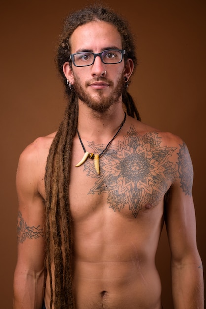 Young handsome Hispanic man with dreadlocks shirtless against br