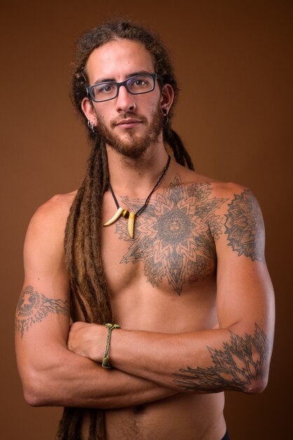 Young handsome Hispanic man with dreadlocks shirtless against br