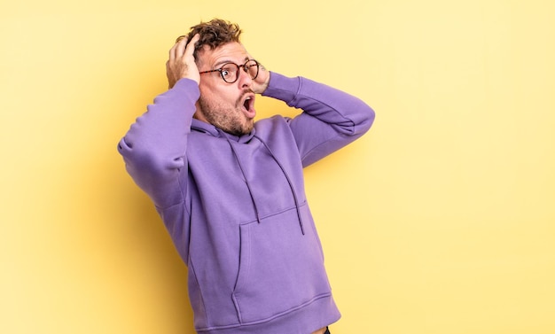 Young handsome hispanic man with open mouth looking horrified and shocked because of a terrible mistake raising hands to head