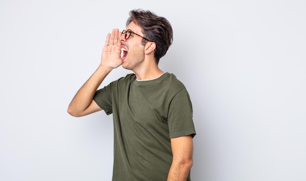 Photo young handsome hispanic man yelling loudly and angrily to copy space on the side, with hand next to mouth