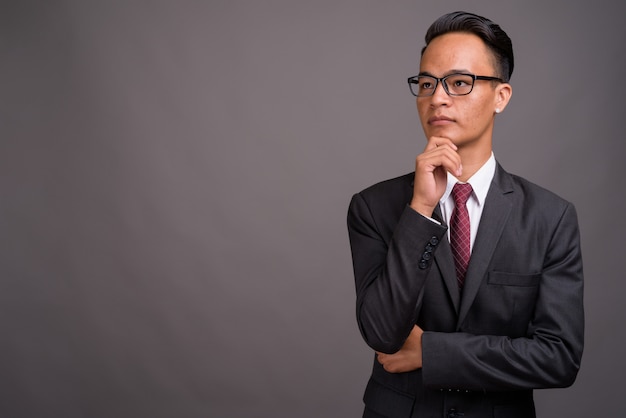 Young handsome Indian businessman against gray wall