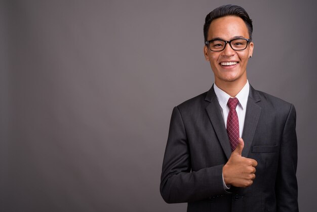 Young handsome Indian businessman against gray wall