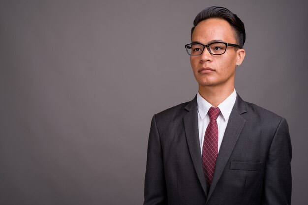 Young handsome Indian businessman against gray wall