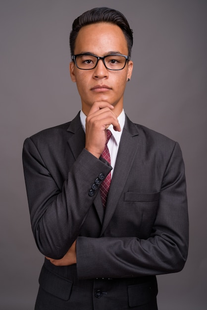 Young handsome Indian businessman against gray wall