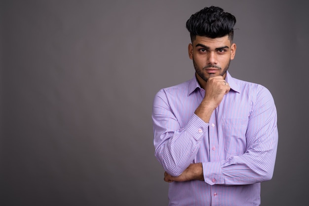  young handsome Indian businessman against gray wall