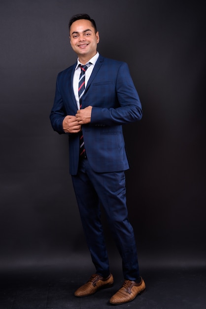  young handsome Indian businessman wearing blue suit against black wall