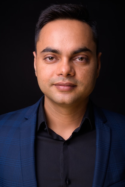  young handsome Indian businessman wearing blue suit against black wall